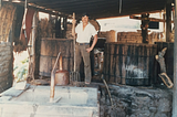 Manuel Santiago Hernandez, my father, in his palenque circa 1984. He’s standing between two wooden vats–used to ferment the mashed agave–holding a pitchfork, February, 1984.