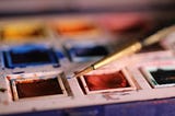 paintbrush dabs into tray of watercolor paints