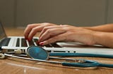 hands typing on laptop keyboard with stethoscope nearby