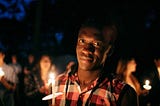 African man holding a candle at a night vigil.