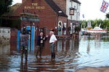 Two men standing in flood water outside a pub.