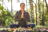 Woman sitting cross legged, hands joined, eyes closed in sitting meditation