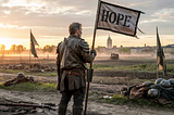 A weathered soldier clad in dark armor stands alone on a dusty battlefield at sunrise. He holds a tattered flag with the word “HOPE” boldly printed across it. Around him, scattered remnants of helmets and gear lie abandoned. In the distance, a town is visible through the mist. His stance is strong and determined, symbolizing leadership resilience, survival after collapse, and the quiet strength required to rebuild a legacy.