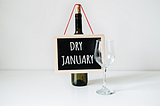 Picture of an empty wine bottle holding a Dry January sign next to an empty win glass.