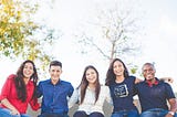 Five friends sitting on a bench with arms around each other