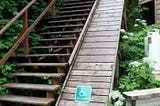 Ridiculous 45 degree staircase ramp with a sign for wheelchair access, next to a wooden staircase