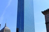 The enormous glass wing of the former John Hancock Tower in Coply Square, Boston. Framed against the blue sky.