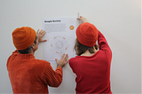 Two colleagues hanging up one of the What the Future Wants posters; photo courtesy of Daisy Kidd