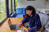 A woman checks off a list while looking at a laptop screen
