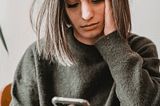 A woman in an olive sweater looking at her phone to know who is calling