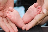 A newborn’s feet are cradled by a parent’s hands.