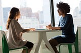 Two professionals talking sit on a round table. 