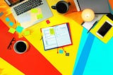 Top view of a laptop, notebook, coffee cups, and post-it notes on a desk