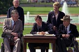 5 people in the image, Bush sitting in the middle and signing the ADA, 2 sitting on a wheelchair, and 2 standing at the back.