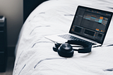 Ableton Live on a laptop sitting on a bed with headphones next to it.