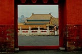 Red wall and a square opening looking through to rooftops at Forbidden City in Beijing, China.