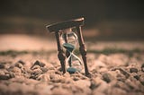 An hourglass with blue sand sits leaning on a bed of rocks, ticking away at this thing we call life.