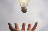 A lit lightbulb hovers above an outstretched hand.