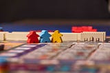 Red, blue, and yellow meeple figures in the game Merv
