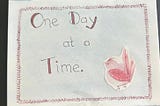 A watercolor bird is pasted to a card that reads “One Day At A Time.”