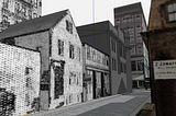 A ground-level view of several buildings on a narrow street in a virtual model, whose facades have been pulled out of old, grainy, halftoned black and white newspaper imagery.