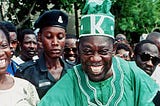 A grinning Alhaji Chief Moshood Kashimawo Olawale Abiola GCFR, Aare Ona Kankafo XIV of Yorubaland, surrounded by supporters.