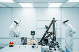 Scientists in a lab wearing full body suits examining equipment