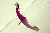 Woman in red dress standing on the beach, her hands over her head as if holding up the world.