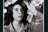 This is the album cover for Cat Power’s Moon Pix LP. It is a black and white picture and features a woman in a denim jacket surrounded by flowers. The text is in red.