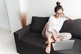 Image of smiling brunette woman typing on laptop while sitting on sofa