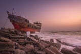 A man sits looking at a wrecked ship on the rocks