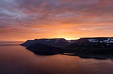 Sunrise coming up over sno capped mountains and reflecting on the water