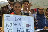 Woman standing in a protest holding a sign that says “I don’t want to die for fashion”