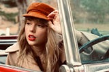 An image of a blonde woman (Taylor Swift) wearing red lipstick sitting in the driver’s seat of a red convertible. She is wearing an orange newsboy cap and a beige coat and her eyes are cast to the side. She has the bill of her cap between her thumb and forefinger. Trees can be seen in the background of the photo.