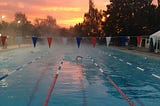 A swimmer swimming towards the camera in the middle of an outdoor pool at sunrise