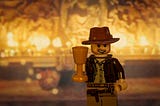 A Lego version of Indiana Jones is posed holding a cup representing the Holy Grail.