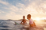 Woman and man surfing in ocean with warm sunlight
