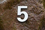 Embossed number five in white color, resting on the wet surface of a boulder.