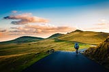 Man on a mountain road cycling towards the rising sun.