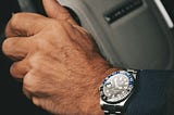 Close-up of a man’s hand wearing an expensive watch and suit.