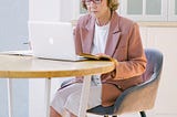 An older woman sitting at the kitchen table and looking at her laptop.