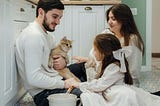 A family holding a cat and mixing dinner on the kitchen floor.