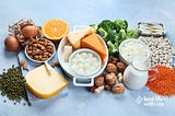 Table laden with almonds, oranges, figs, sardines, lentils, broccoli, and yes cheese. Image Source Canva Pro.