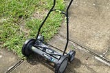 Hand powered rotary lawnmower sitting on a driveway.