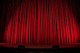 A closed red curtain on an empty theater stage