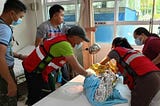 Philippine Red Cross workers workers putting a child wrapped in an emergency blanket on a hospital bed