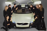 The nine women, all dressed in black, and the greenish, gull-winged YCC car that they designed.