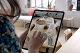 A picture of a woman who’s using an AR on iPad to place virtual food on the real table