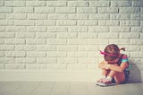 A young girl sits alone with head hung down against a brick wall