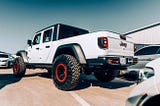 White Jeep Gladiator with red-accented wheels parked at a car auction facility.